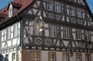 Un edificio tradicional con entramado de madera, con varias ventanas y una estructura metálica decorativa en la fachada.