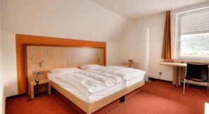 Une chambre d’hôtel avec un lit simple, une petite table de chevet, une chaise et une fenêtre avec des rideaux.