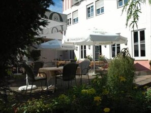Un espace extérieur aménagé avec des tables, des chaises et des parasols, avec un bâtiment en arrière-plan.
