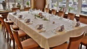 A dining table set for a meal with chairs around it, a window with a view of the street, and a vase with flowers on the table. - Landgasthof Hirsch (Remshalden)