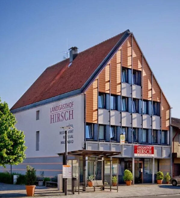 Un hôtel au design moderne, avec une enseigne bien visible indiquant « Landgasthof Hirsch » et un espace d’entrée abrité.