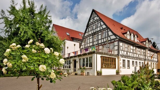 A traditional half-timbered building with a red roof, large windows, and a garden with white flowers. - Landgasthof Hirsch (Remshalden)