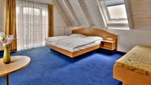 A bedroom with a sloped ceiling, a bed, a bedside table, a small table with a vase, and a window. - Landgasthof Hirsch (Remshalden)
