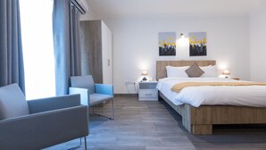 A modern hotel room with a bed, a chair, a nightstand, and two wall art pieces. - Villandro Residence (Accra)