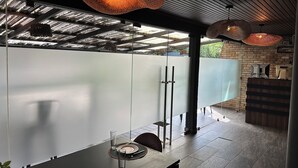 A modern dining area with a glass partition, hanging pendant lights, and a brick wall. - Villandro Residence (Accra)