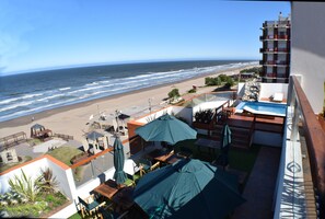 A balcony with a view of the beach, outdoor seating, and a pool area. - Apartamentos JR (San Bernardo del Tuyú)