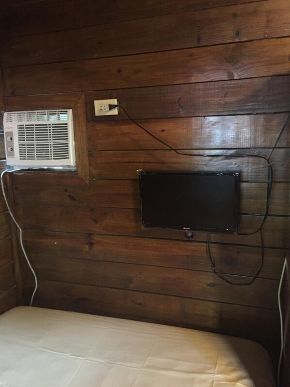 A wooden cabin room with a bed, an air conditioning unit, and a television mounted on the wall.