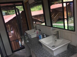 A bathroom with two sinks, a mirror, and a view of a wooden building outside. - Cabañas Colindas (Panama City)