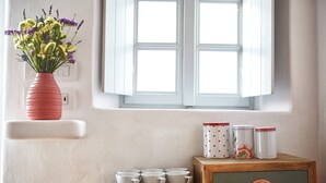 A room with a window, a vase with flowers, and a wooden cabinet with kitchenware. - Santorini-treasures Rockside Villa traditional (Emporio)