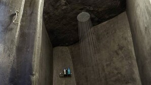 A narrow, dimly lit shower area with a circular skylight overhead and a handheld showerhead. - Santorini-treasures Rockside Villa traditional (Emporio)