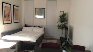 A modern bedroom with a bed, a desk, and a potted plant.