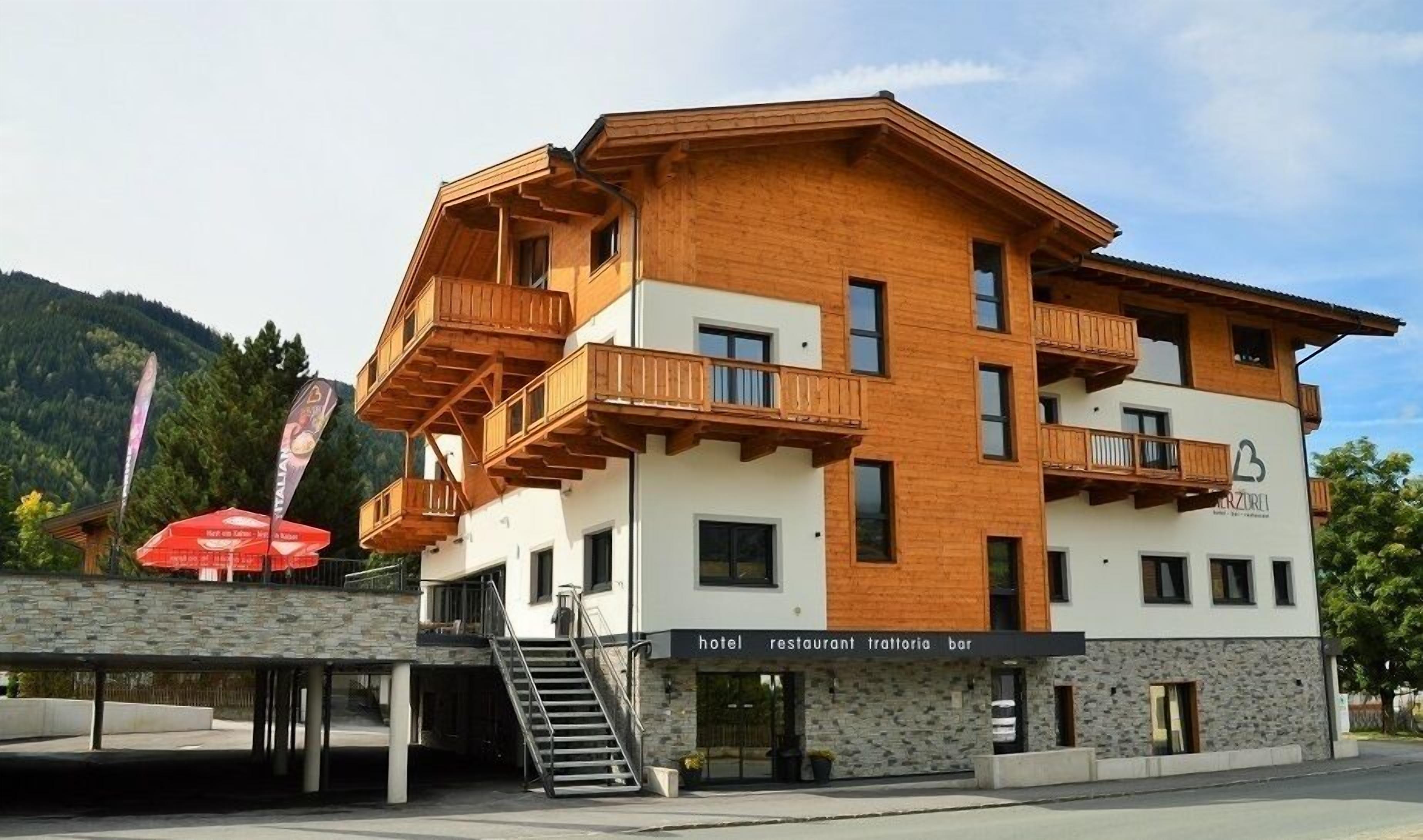 A multi-story building with wooden balconies, a stone facade, and a sign indicating it houses a hotel, restaurant, trattoria, and bar.