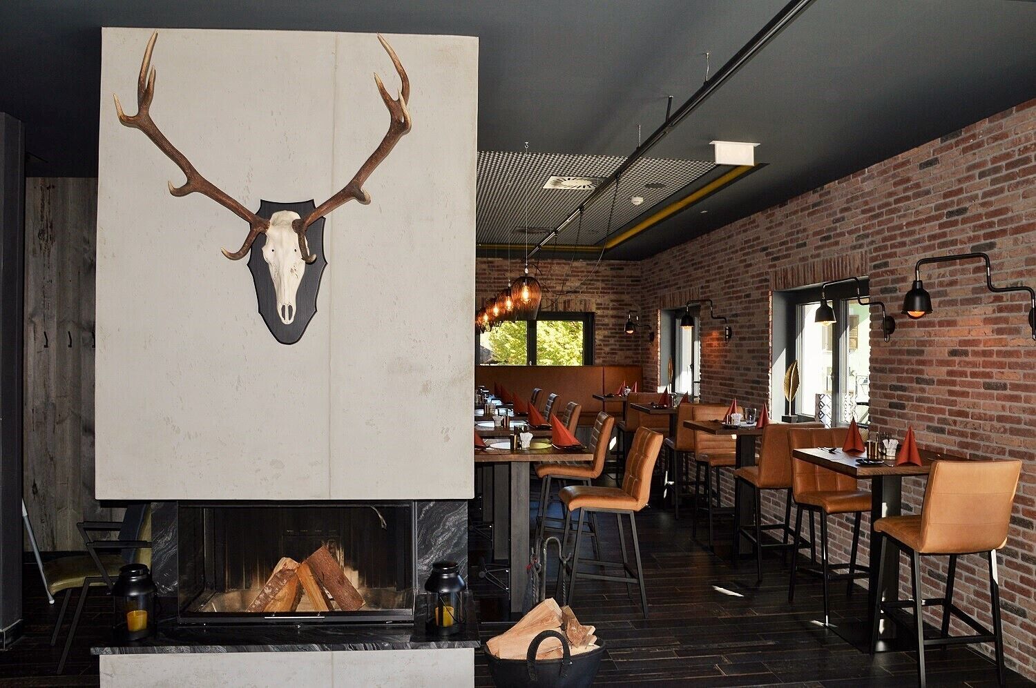 A restaurant with a rustic brick wall, a fireplace with a deer skull decoration, and modern lighting fixtures.