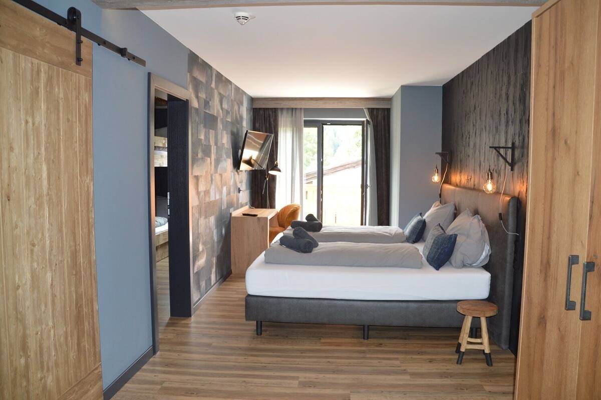 Ein modernes Schlafzimmer mit einem großen Bett, Holzboden und Blick ins Freie.