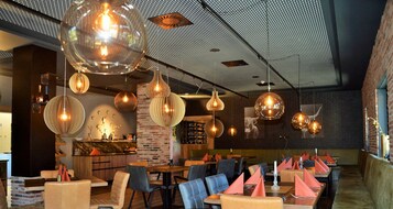 Interior de restaurante con mesas redondas, sillas y lámparas esféricas colgantes.