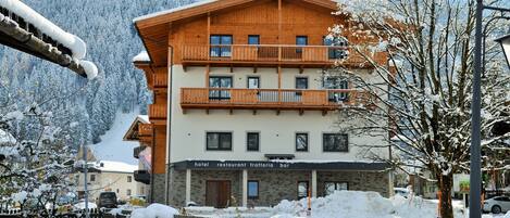 A multi-story wooden building with balconies, a sign indicating it houses a hotel, restaurant, trattoria, and bar.