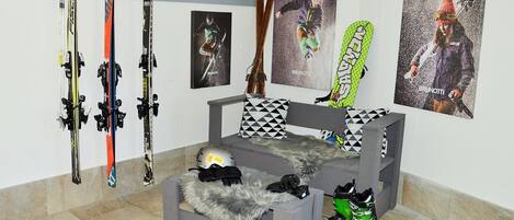 A room with a grey sofa, a fur throw, and a helmet on a table. There are skis and a snowboard leaning against the wall.