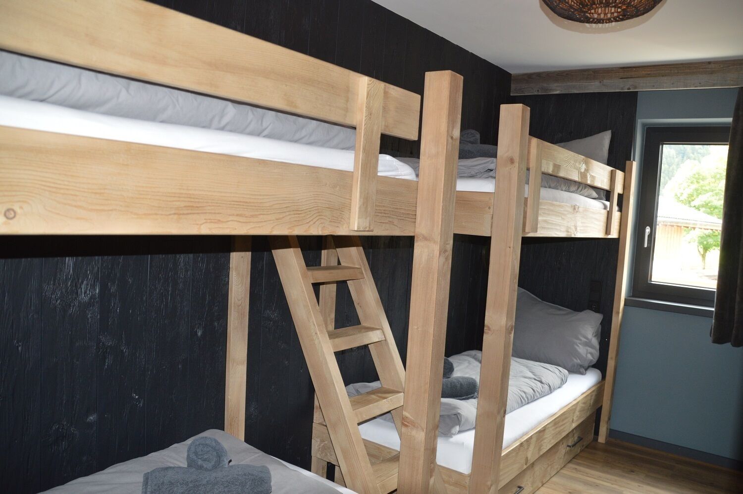 Een slaapkamer met stapelbed, een ladder, houten wanden en een raam met gordijnen.