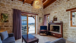 Una habitación con paredes de piedra, techo de madera, chimenea, televisor y vistas al exterior.