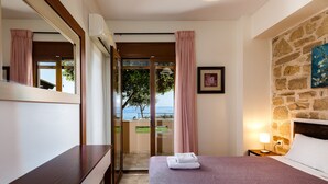 Habitación de hotel con cama, escritorio, mesita de noche, lámpara, marco de fotos y vista al mar a través de una puerta de vidrio.