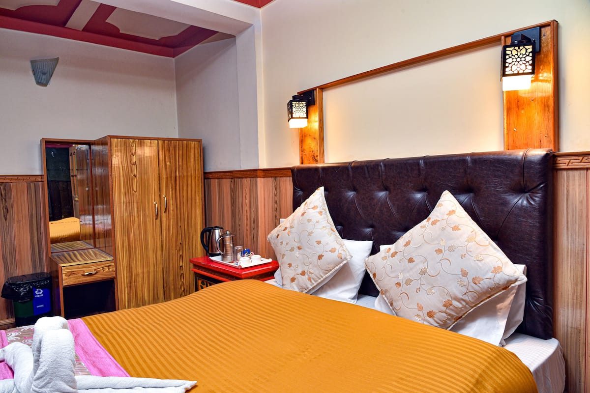A hotel room with a large bed, wooden wardrobe, and a nightstand with a lamp.