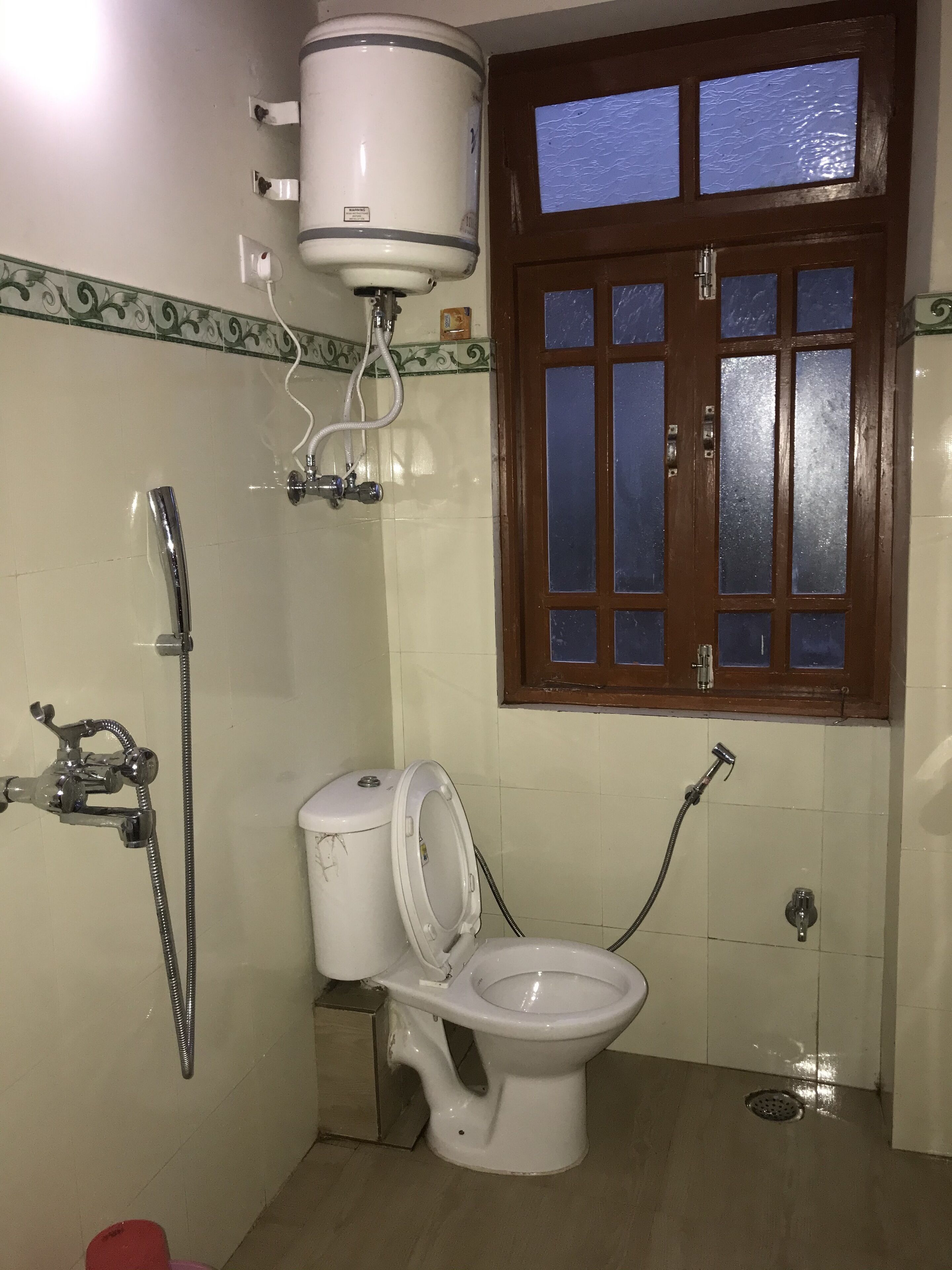 A bathroom with a toilet, a shower, and a window.