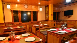 A restaurant with wooden furniture, tables set for dining, and a clock on the wall. - Rufina Blue Pine (Chungthang)