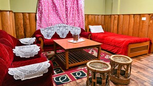 A room with a wooden bed, a red sofa, a small table with a glass, and two wicker stools. - Rufina Blue Pine (Chungthang)