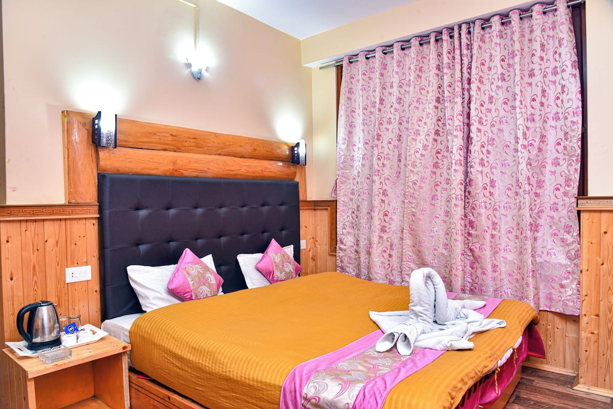 A neatly made bed with a wooden headboard, a bedside table with a kettle, and a floral curtain.