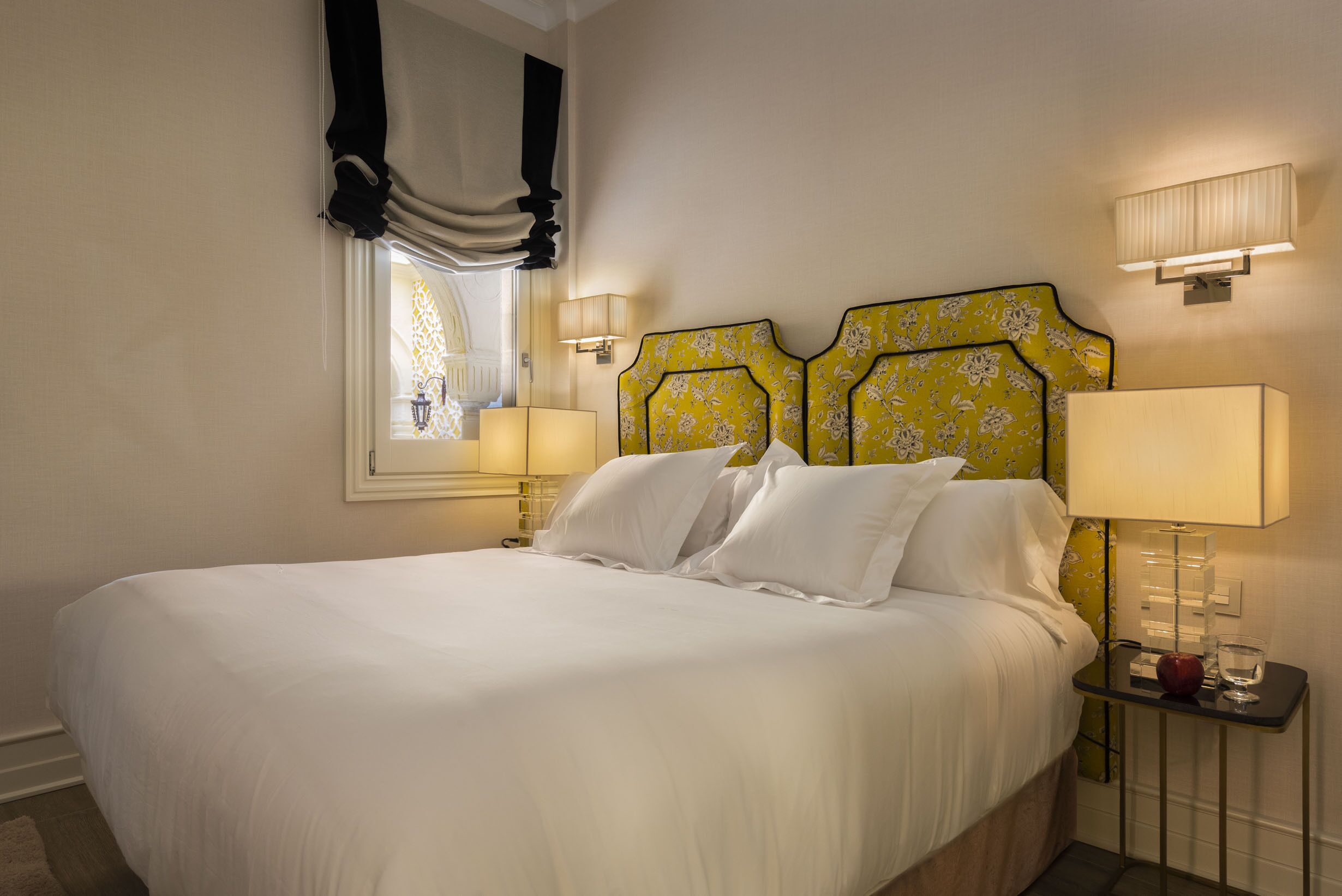 A neatly made bed with white linens, a headboard with a floral pattern, and bedside lamps on either side.