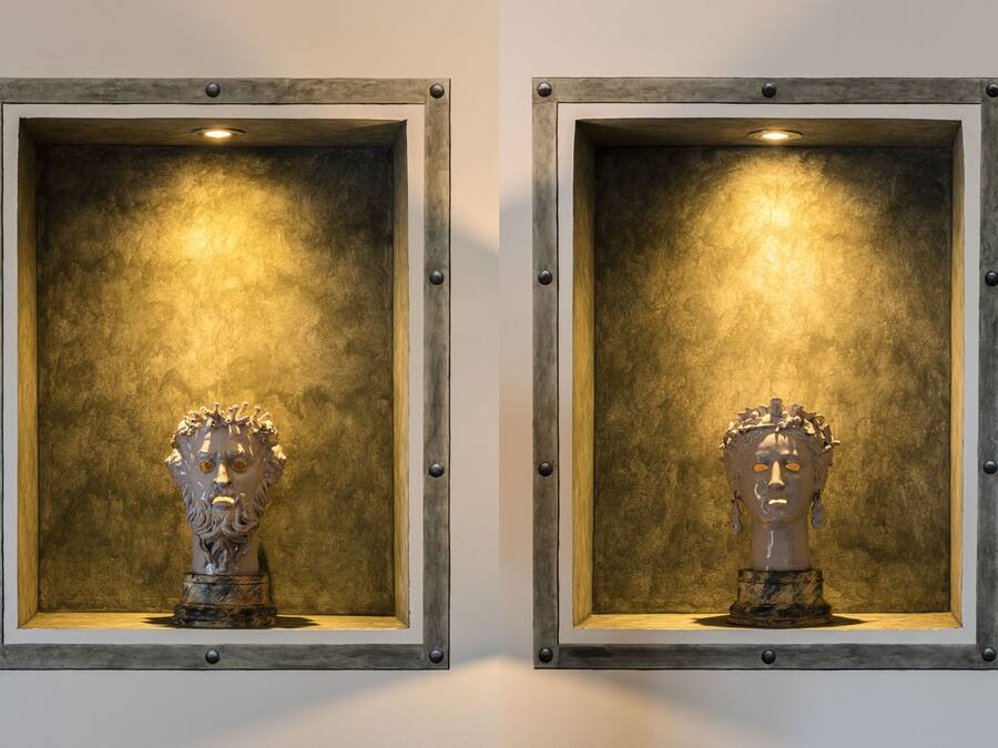Duas esculturas de busto idênticas em expositores emoldurados, com um fundo texturizado.