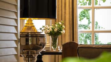 A lamp with a black shade, a vase with flowers, and a window with greenery outside.