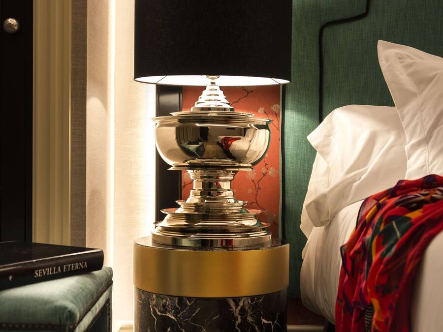A modern hotel room with a marble-patterned floor lamp, a green upholstered headboard, and a neatly made bed with a white pillow and a colorful throw blanket.