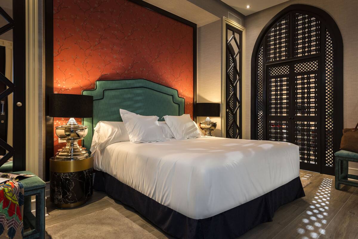 Een net opgemaakt bed met witte lakens, een blauwgroen hoofdbord en twee nachtkastjes met lampen.