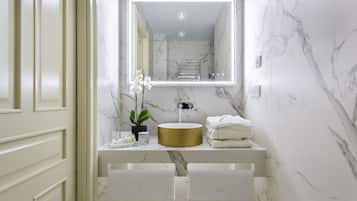 A bathroom with a marble wall, a gold sink, and a mirror with LED lighting.