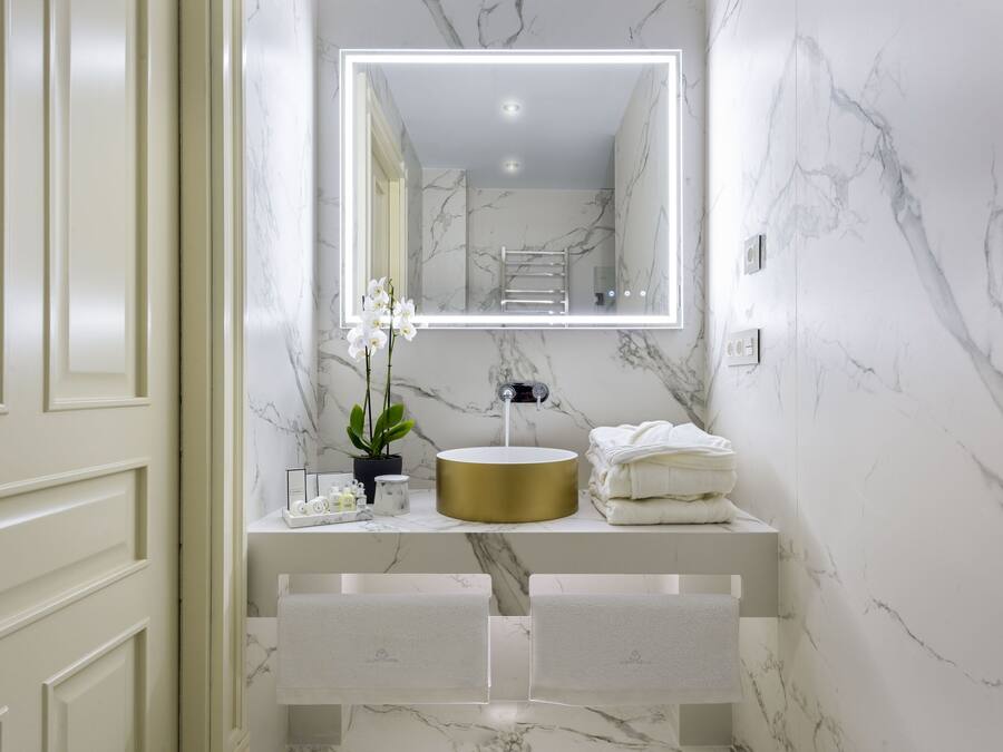 A bathroom with a marble wall, a gold sink, and a mirror with LED lighting.