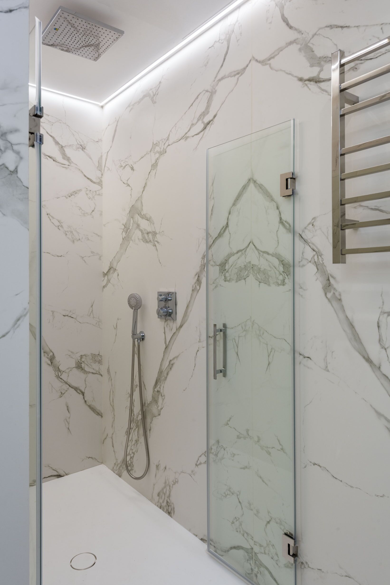 A modern bathroom with a glass shower enclosure, marble-patterned walls, and a glass door.