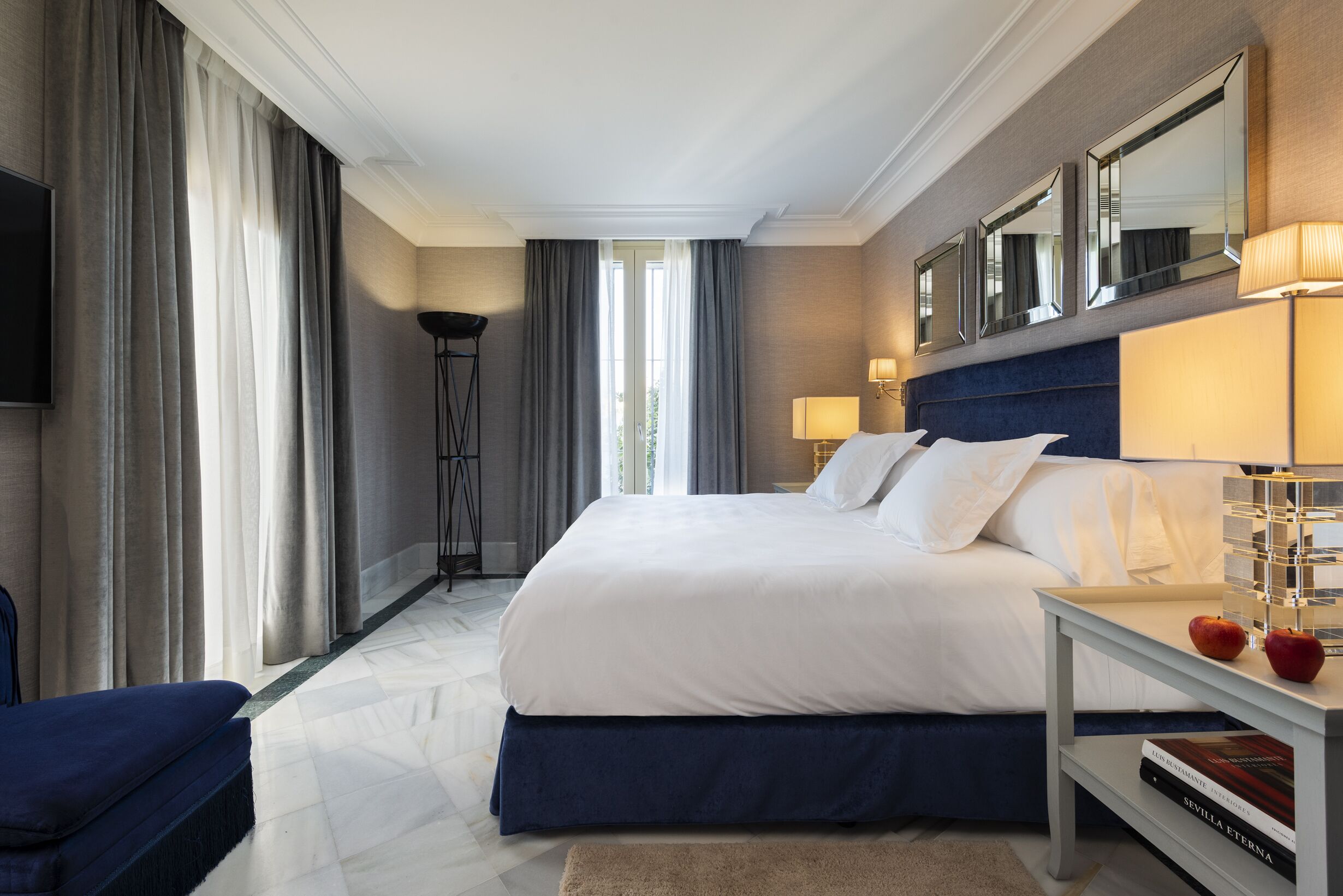 A hotel room with a large bed, a bedside table with a lamp, a chair, and a flat-screen TV mounted on the wall.