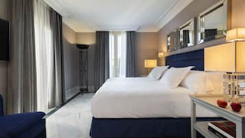 A hotel room with a large bed, a bedside table with a lamp, a chair, and a flat-screen TV mounted on the wall.