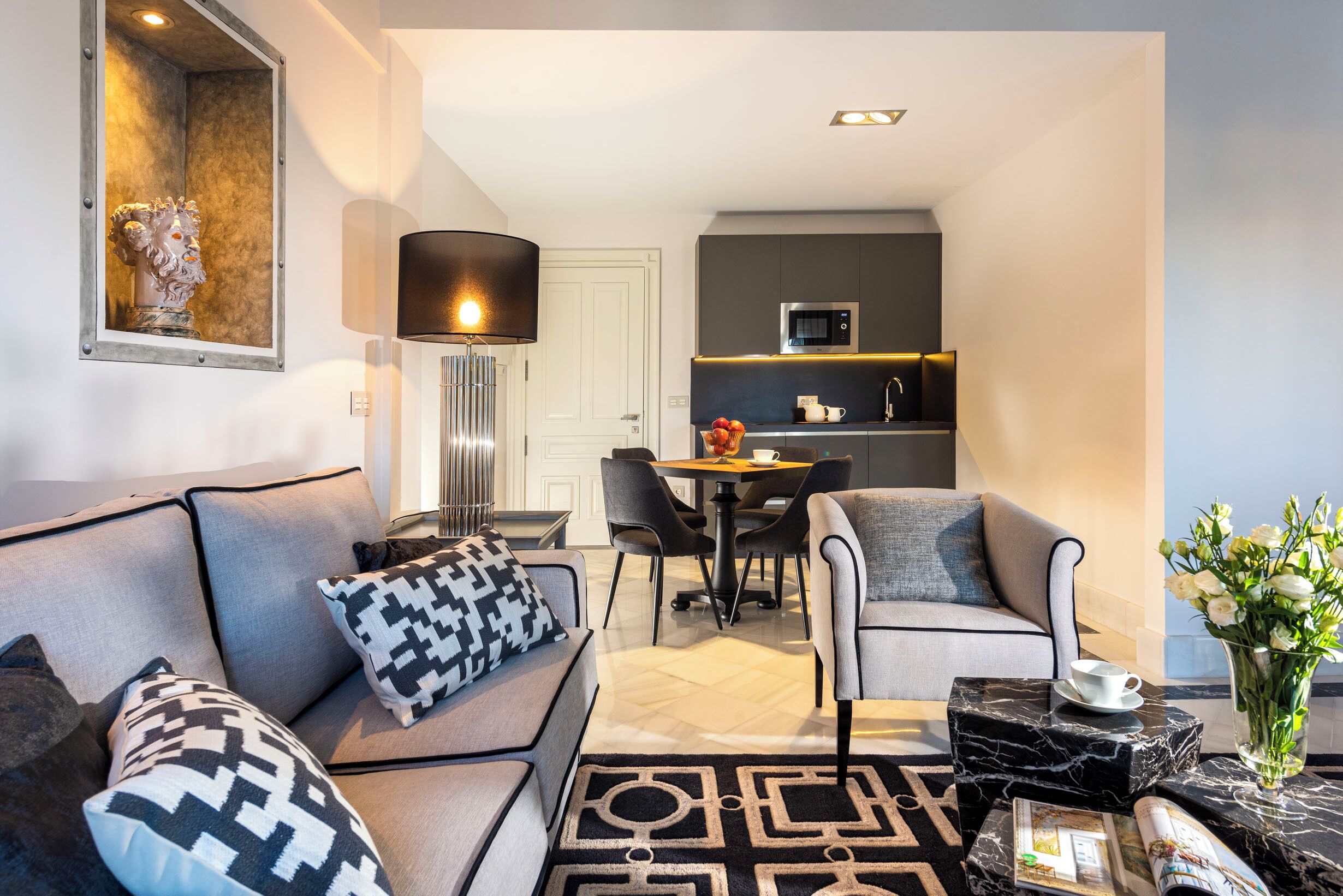 A modern living room with a sofa, armchairs, a coffee table, and a dining area with a table and chairs.