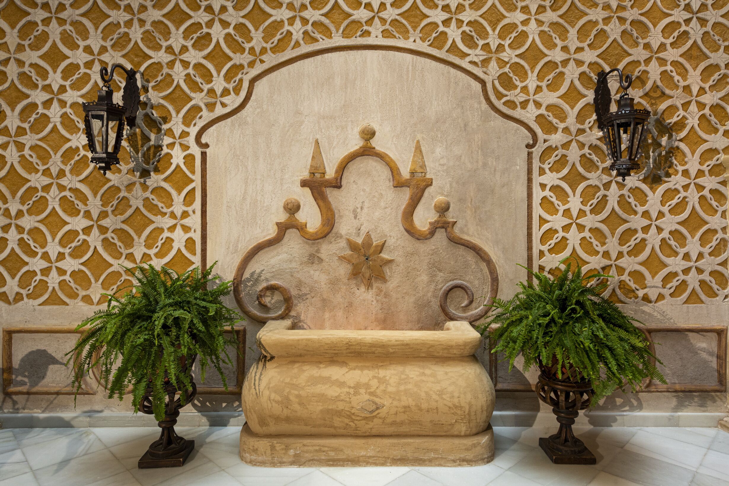 Un vestíbulo con una pared decorativa, un cabecero grande y ornamentado, y dos plantas en macetas.