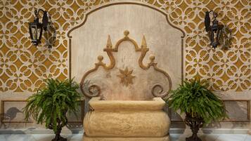 Un vestíbulo con una pared decorativa, un cabecero grande y ornamentado, y dos plantas en macetas.