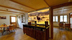 Una habitación amplia con pisos de madera, una gran mesa de comedor de madera y una zona de cocina con mostrador y armarios de madera.