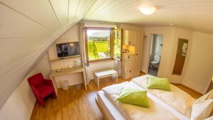Un dormitorio con cama, escritorio, televisor y ventana con vistas a la vegetación.