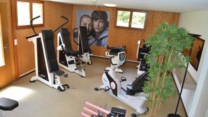 Un gimnasio con diversas máquinas de ejercicio, un cartel grande en la pared y una planta en maceta.