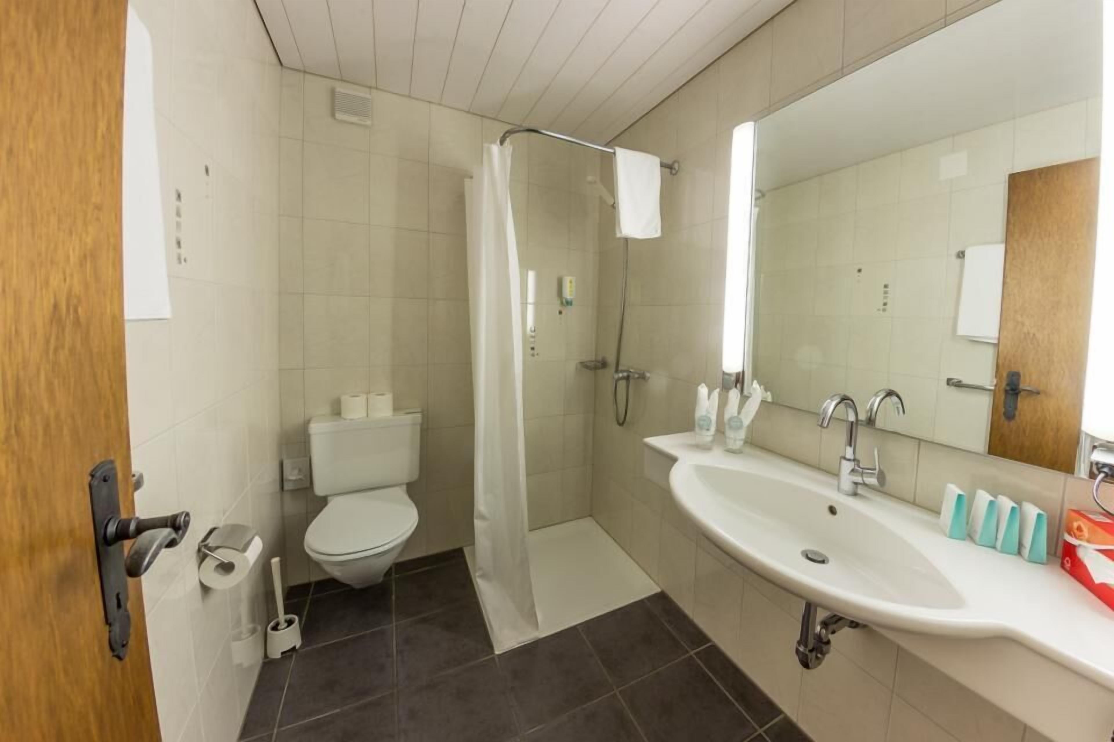 A bathroom with a toilet, shower, sink, and mirror.
