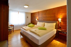 Una cama doble con dos almohadas, una mesita de noche con lámpara y cabecero de madera.