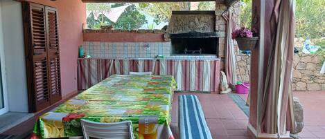 An outdoor patio with a table set for dining, a grill, and a stone wall.