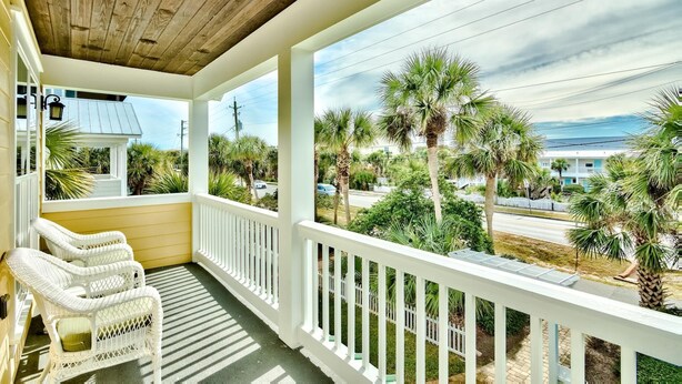 A covered porch with white wicker chairs, a wooden ceiling, and a view of palm trees and a road. - Gulf Views with Pool and Sun Deck Space (Destin)