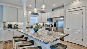 A modern kitchen with white cabinets, a granite island with bar stools, stainless steel appliances, and pendant lighting. - Gulf Views with Pool and Sun Deck Space (Destin)